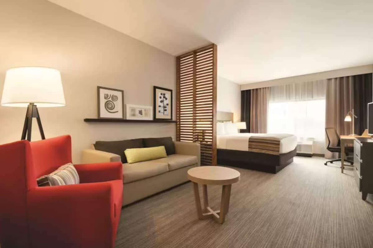 Ein Hotelzimmer mit einem Bett, einem roten Sessel, einer Couch, einem runden Tisch, einem Schreibtisch und einem Fernseher.