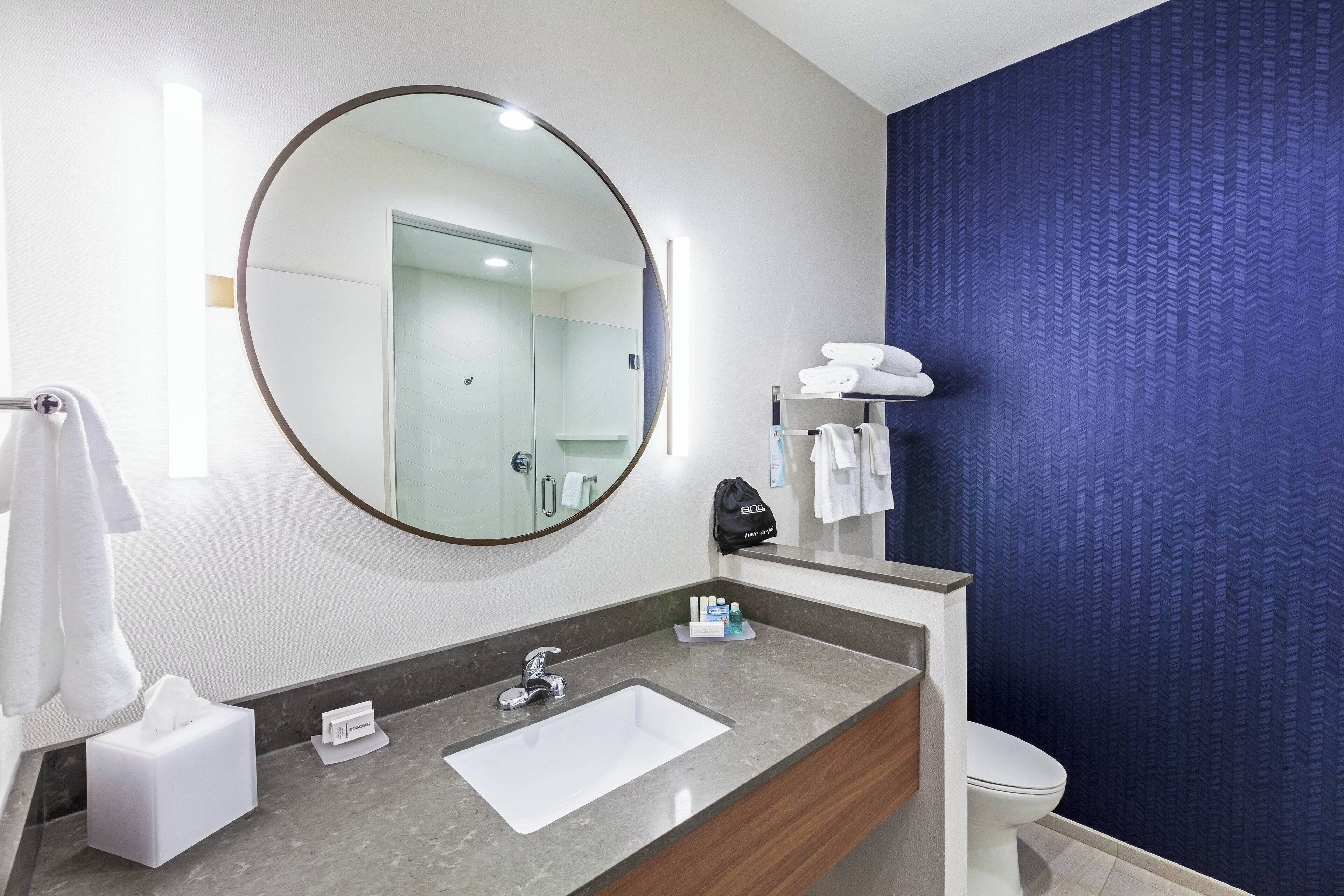 Een badkamer met een ronde spiegel, een wastafel, een toilet en een handdoekrek.