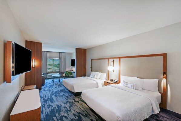 A hotel room with two beds, a flat-screen TV, a desk, and a view of the outdoors.