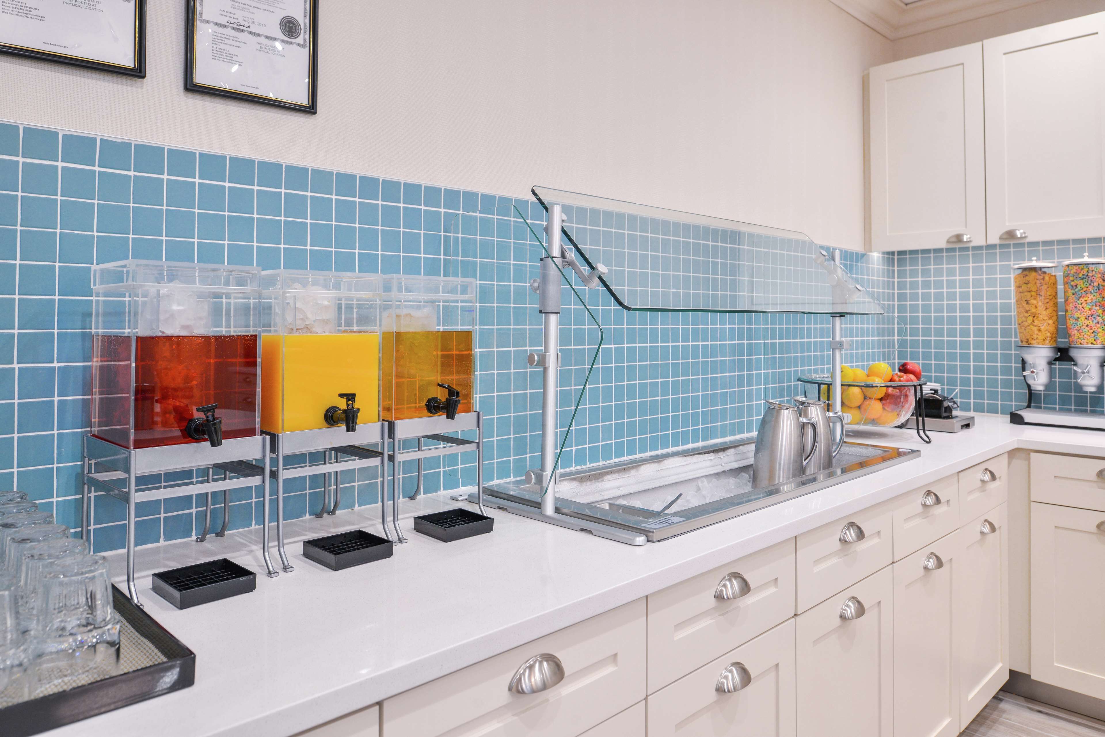 A kitchen with a blue tiled backsplash, a coffee station, and a fruit display.