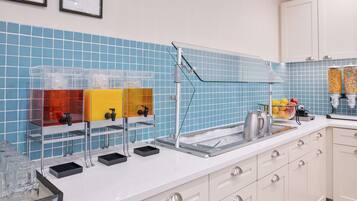 A kitchen with a blue tiled backsplash, a coffee station, and a fruit display.