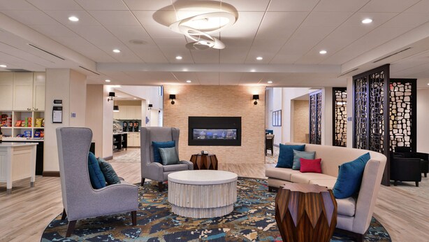 A modern hotel lobby with a round coffee table, sofas, and a TV mounted on the wall.