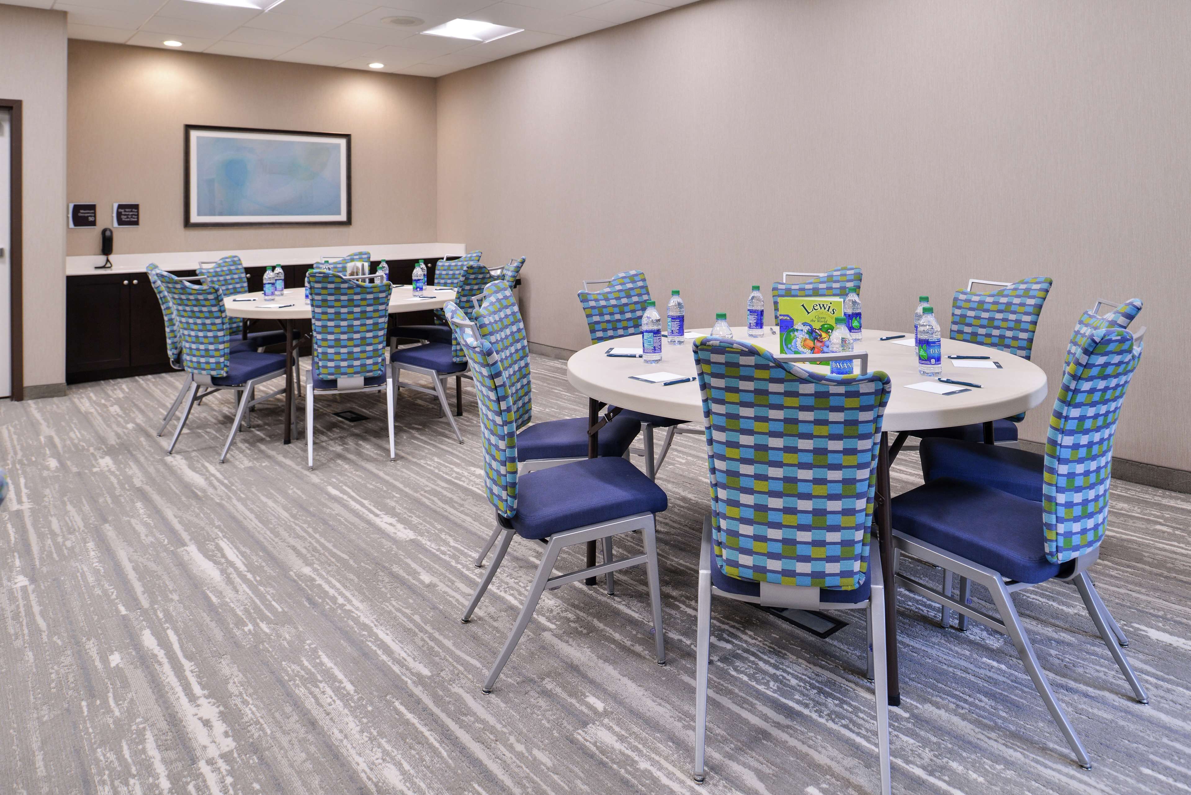 A conference room with round tables, blue and green checkered chairs, and water bottles on the tables.