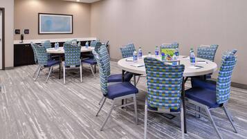 A conference room with round tables, blue and green checkered chairs, and water bottles on the tables.