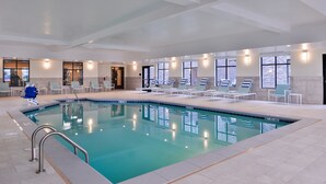 An indoor swimming pool with clear water, surrounded by lounge chairs and a tiled floor.