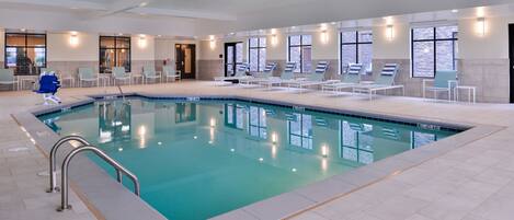 Una piscina interior con agua cristalina, rodeada de sillones de descanso y suelo de baldosas.