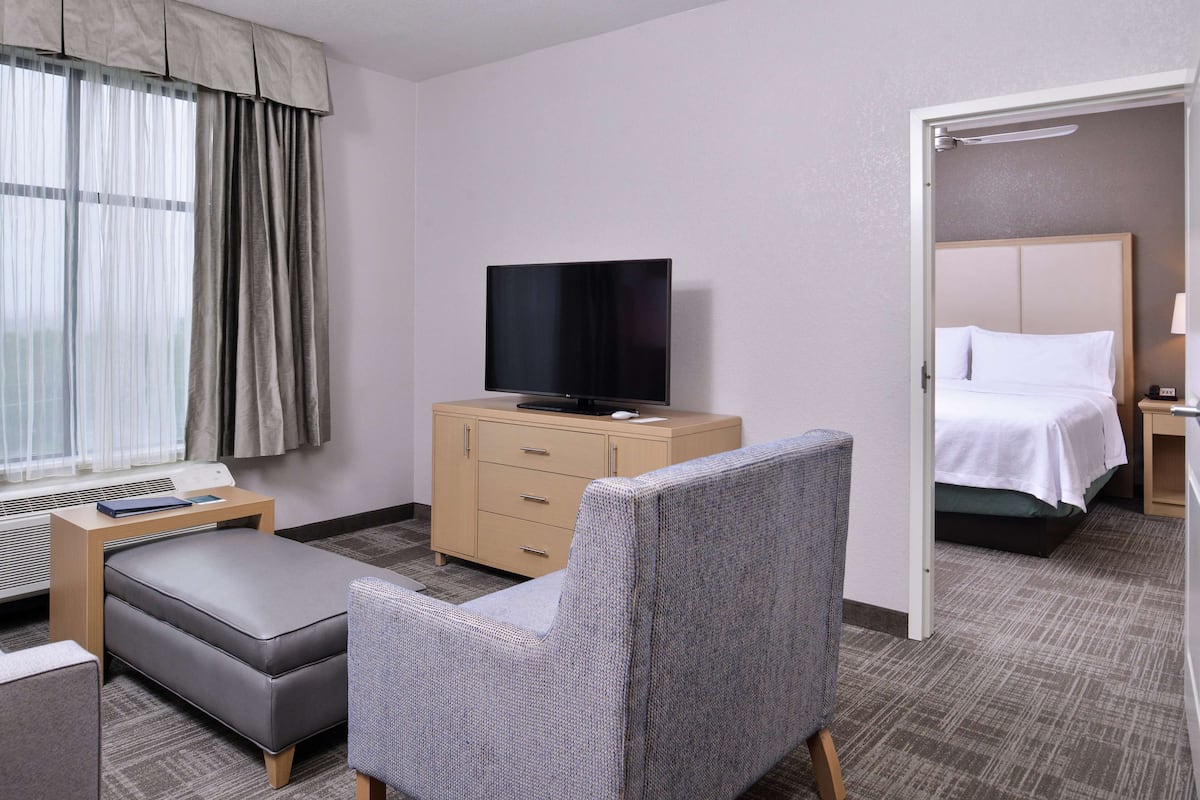 Una habitación de hotel con una cama, un televisor en una cómoda, una silla y un escritorio con una lámpara.