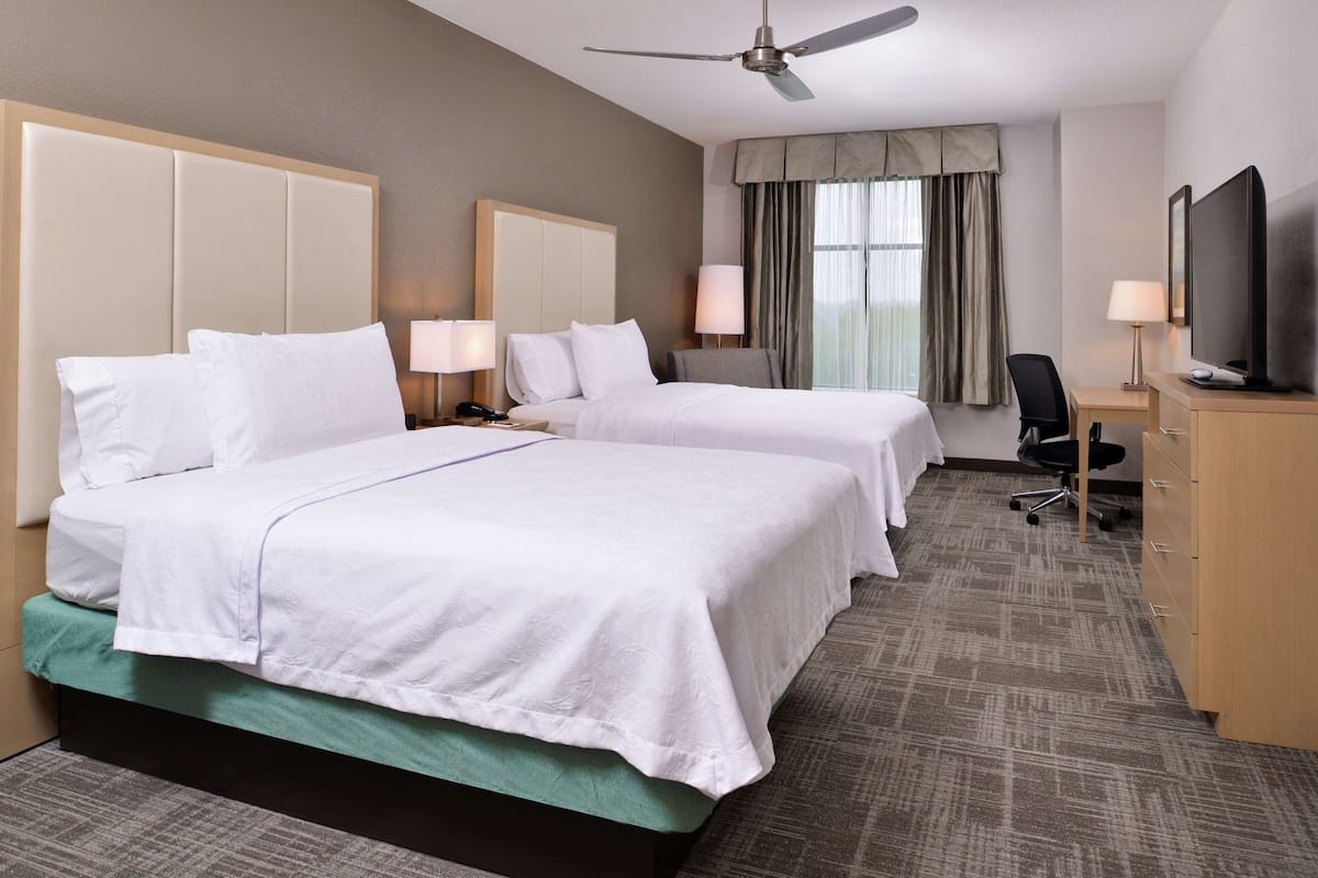 Habitación de hotel con dos camas, un escritorio, una silla, un televisor y un ventilador de techo.