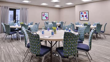 A conference room with round tables, blue and green checkered chairs, water bottles, and framed abstract art on the walls.