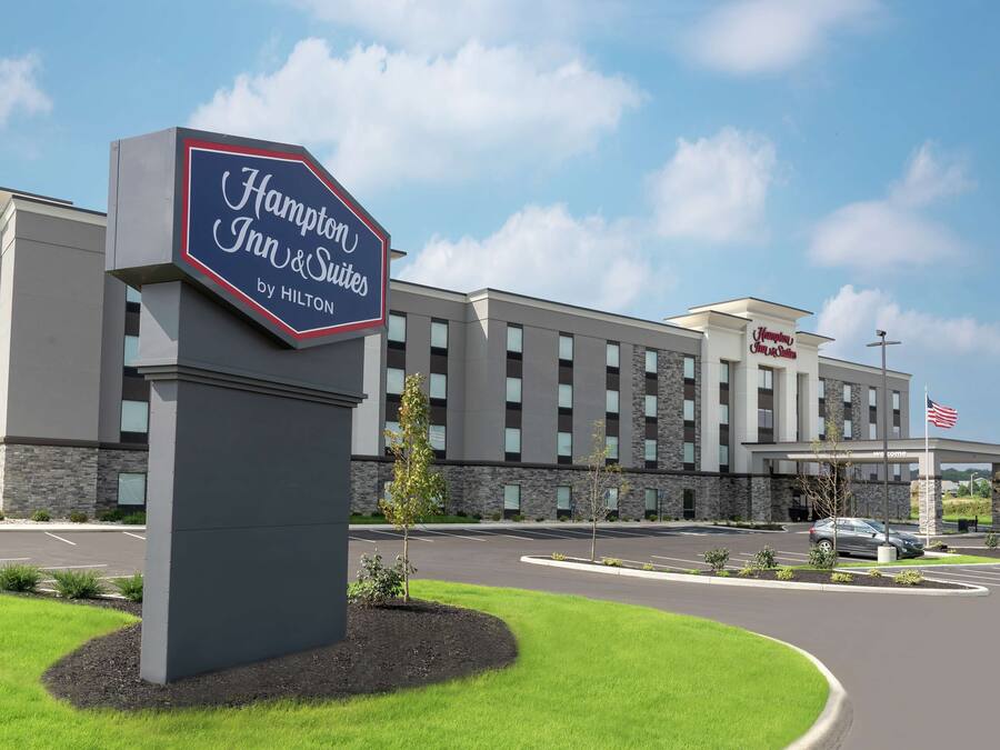 A Hampton Inn & Suites by Hilton hotel with a modern design, a welcoming entrance, and a clear sky.