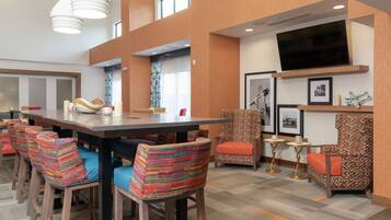 A modern dining area with a long table, colorful chairs, and a flat-screen TV mounted on the wall.