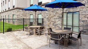 An outdoor patio area with stone walls, a black metal fence, and tables with chairs. - Hampton Inn & Suites Xenia Dayton (Xenia)