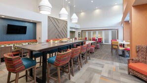 A modern hotel lobby with a long communal table, colorful bar stools, and a television mounted on the wall. - Hampton Inn & Suites Xenia Dayton (Xenia)