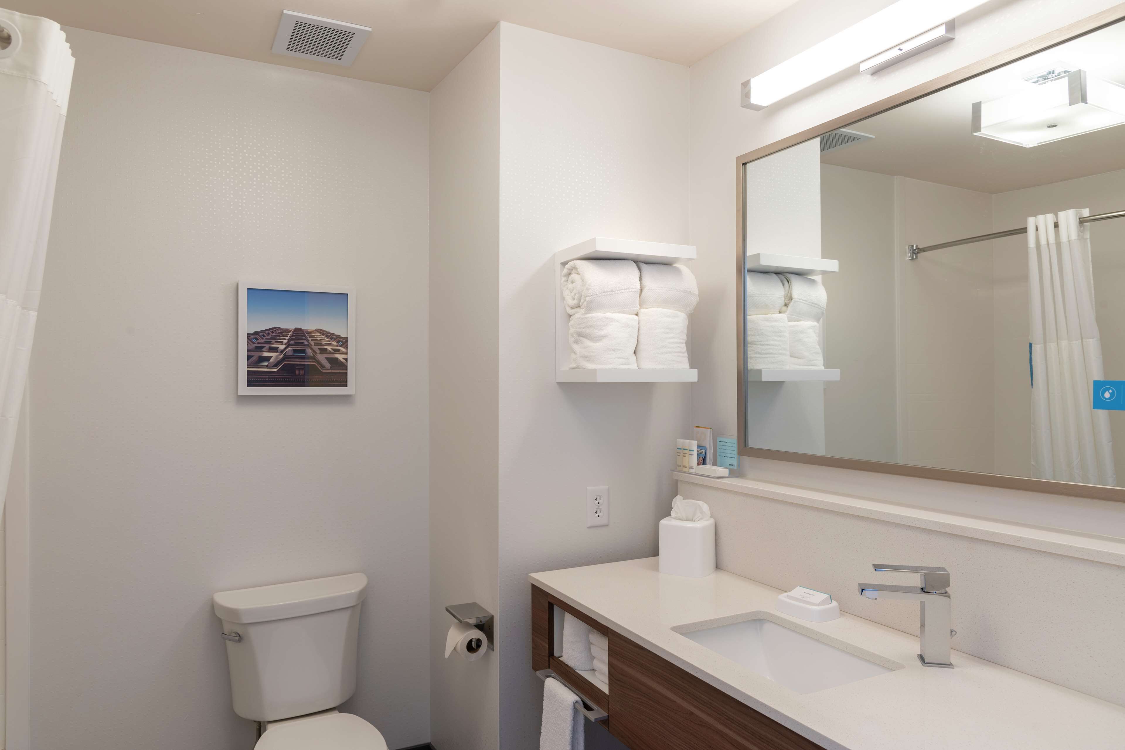 A modern bathroom with a toilet, sink, and a large mirror. There are towels and toiletries on the counter.
