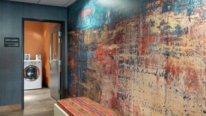 A hotel room with a large abstract mural, a washing machine, and a bench with a colorful cushion. - Hampton Inn & Suites Xenia Dayton (Xenia)