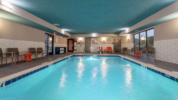An indoor swimming pool with a blue tiled edge, surrounded by lounge chairs and a hexagonal tile wall. - Hampton Inn & Suites Xenia Dayton (Xenia)