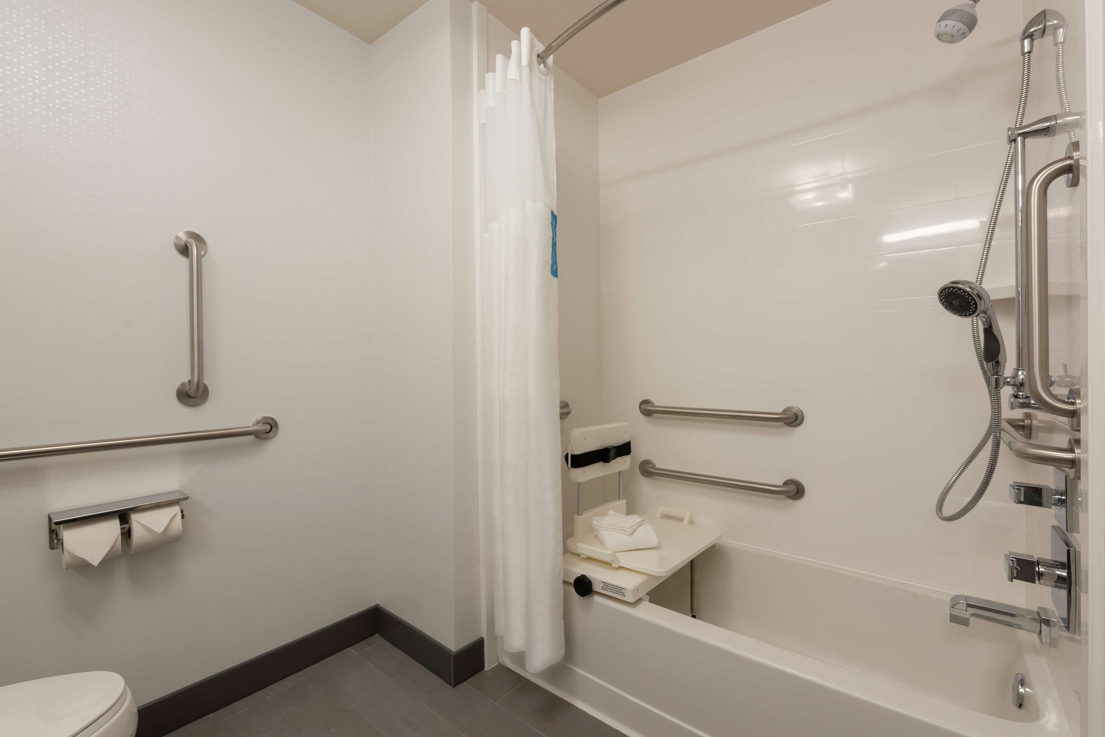 Ein Badezimmer mit Dusche, Haltegriffen, Toilette und Handtuchhalter.