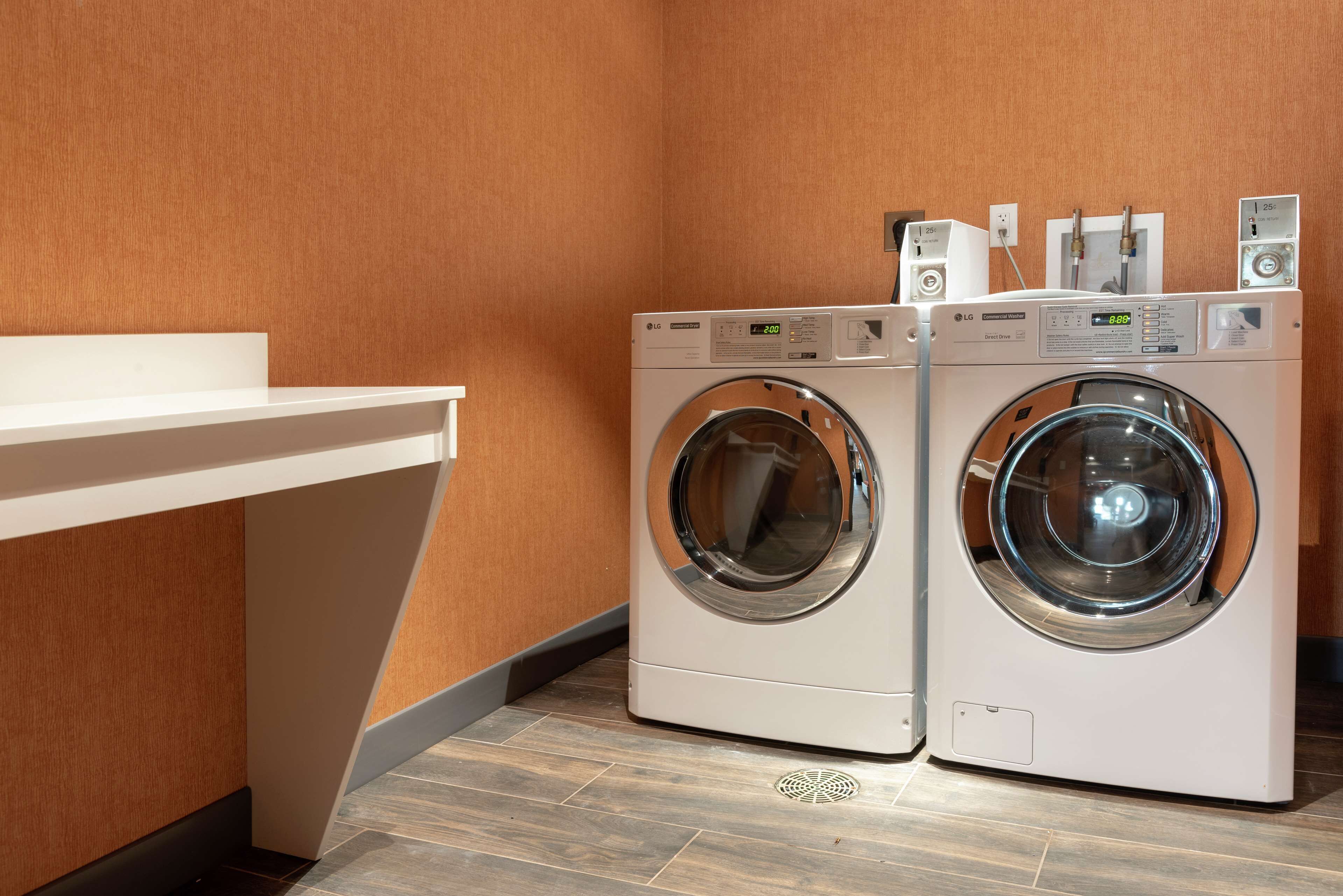 A laundry area with two front-loading washing machines, a white countertop, and a wooden floor.