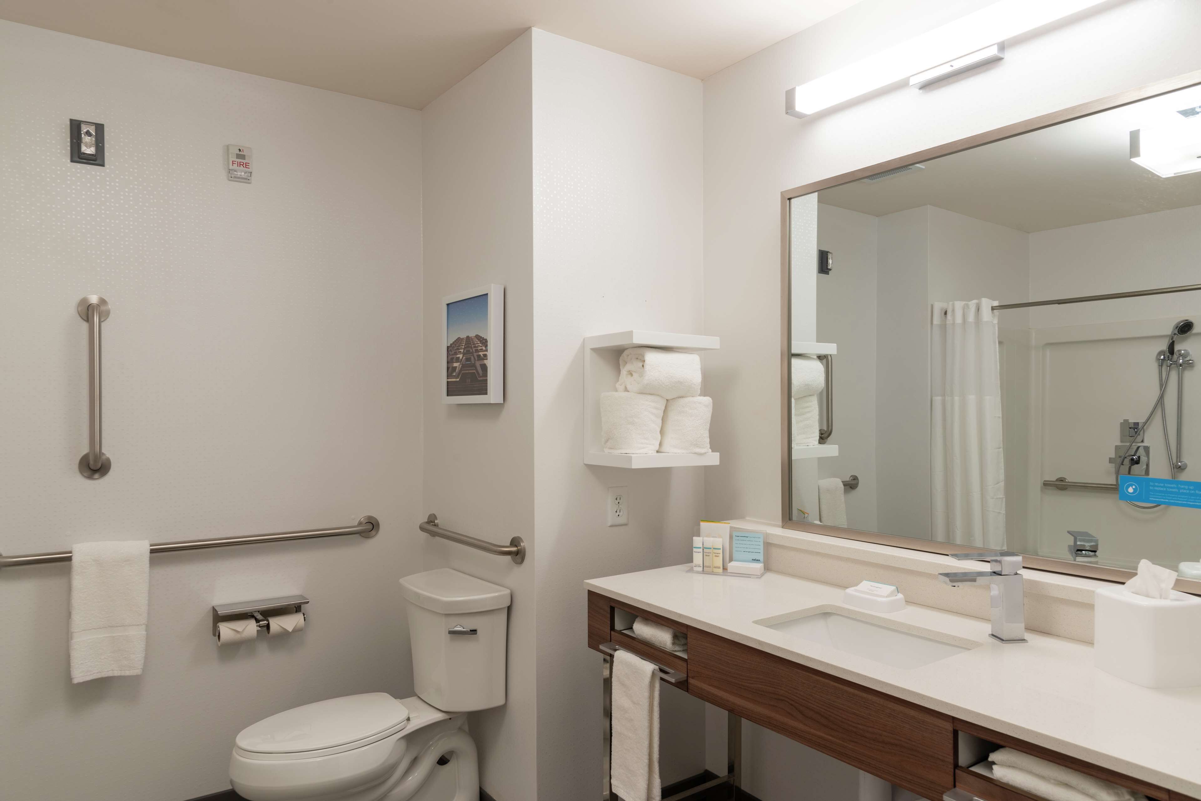 Un baño moderno con inodoro, bidé, barras de apoyo, un espejo grande y un lavabo con tocador.