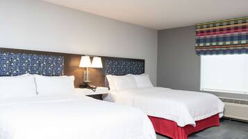 Habitación de hotel con dos camas, una mesita de noche con lámpara, cabecera estampada y ventana con cortina colorida.