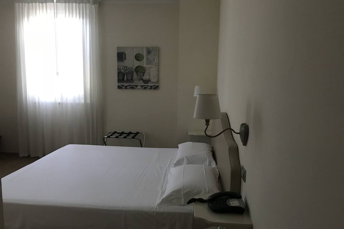 A hotel room with a large bed, a bedside lamp, a telephone, and a painting on the wall.