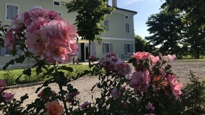 A large building with a symmetrical facade, a central entrance, and a well-maintained garden with pink flowers. - Villa Pepoli (Occhiobello)