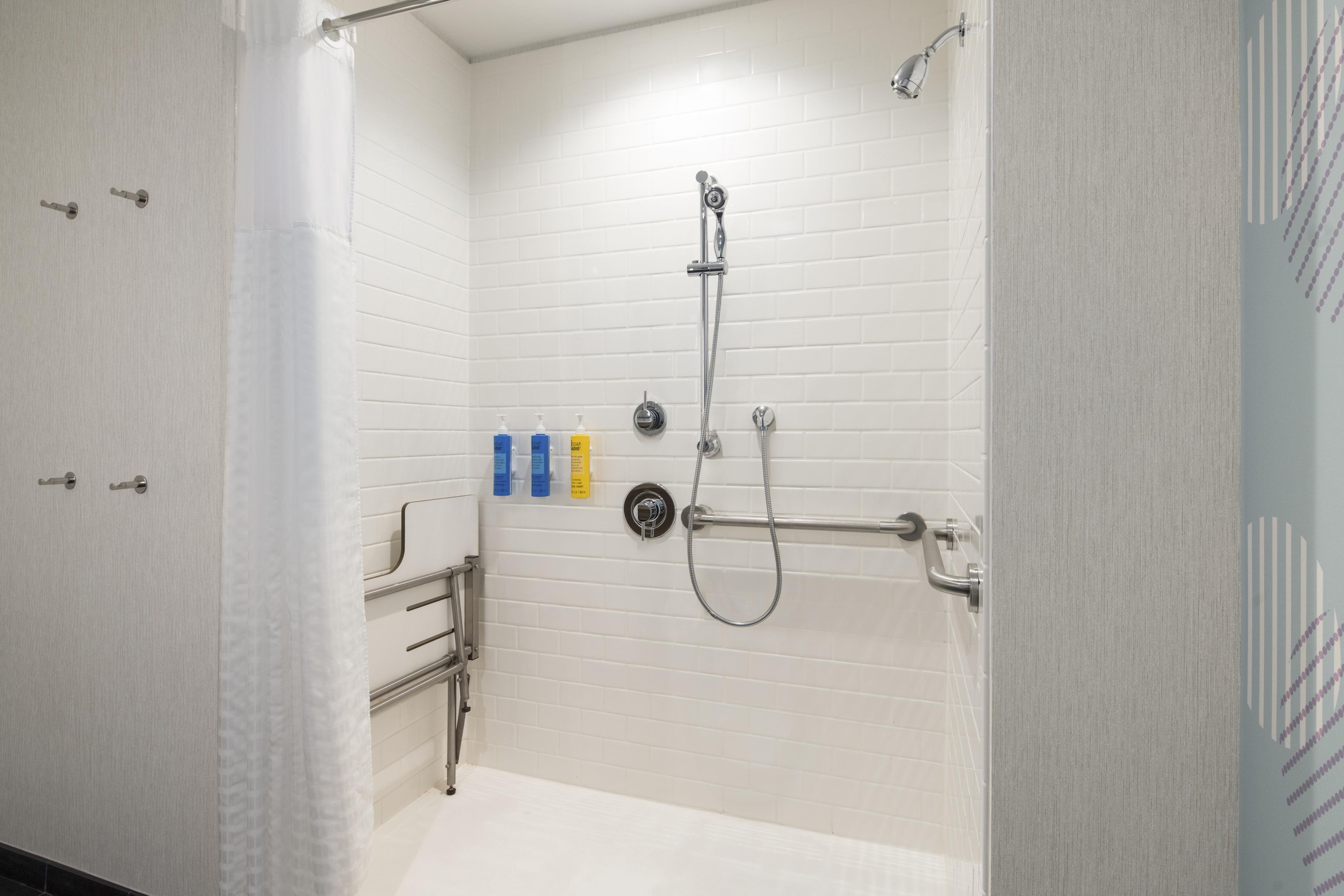 A walk-in shower with white tiled walls, a handheld showerhead, a handheld shower attachment, and a towel rack.