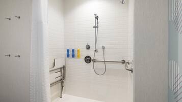 A walk-in shower with white tiled walls, a handheld showerhead, a handheld shower attachment, and a towel rack.