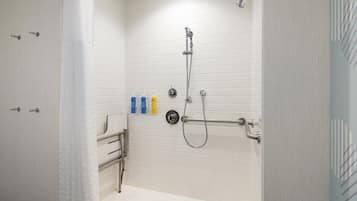 Une douche à l’italienne avec des murs recouverts de carreaux blancs, une pomme de douche à main et un flexible de douche, ainsi qu’un porte-serviettes.