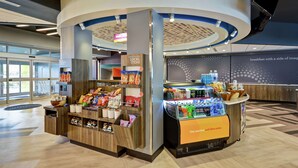 A food kiosk with a variety of snacks and beverages, a sign for local items, and a counter with a beverage display. - Tru by Hilton Chicopee Springfield (Chicopee)