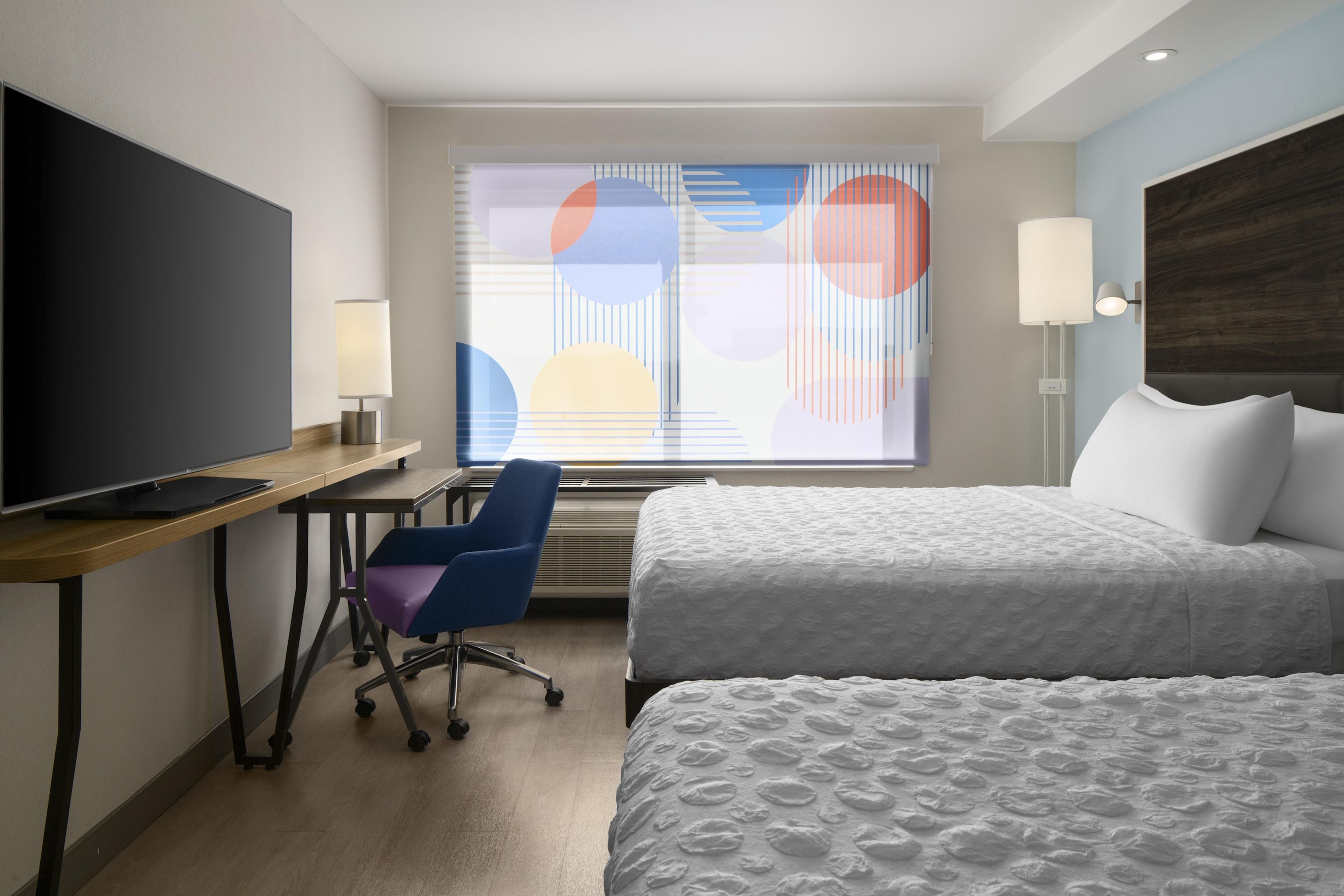 Habitación de hotel con cama, escritorio con silla, televisor y ventana con vista.