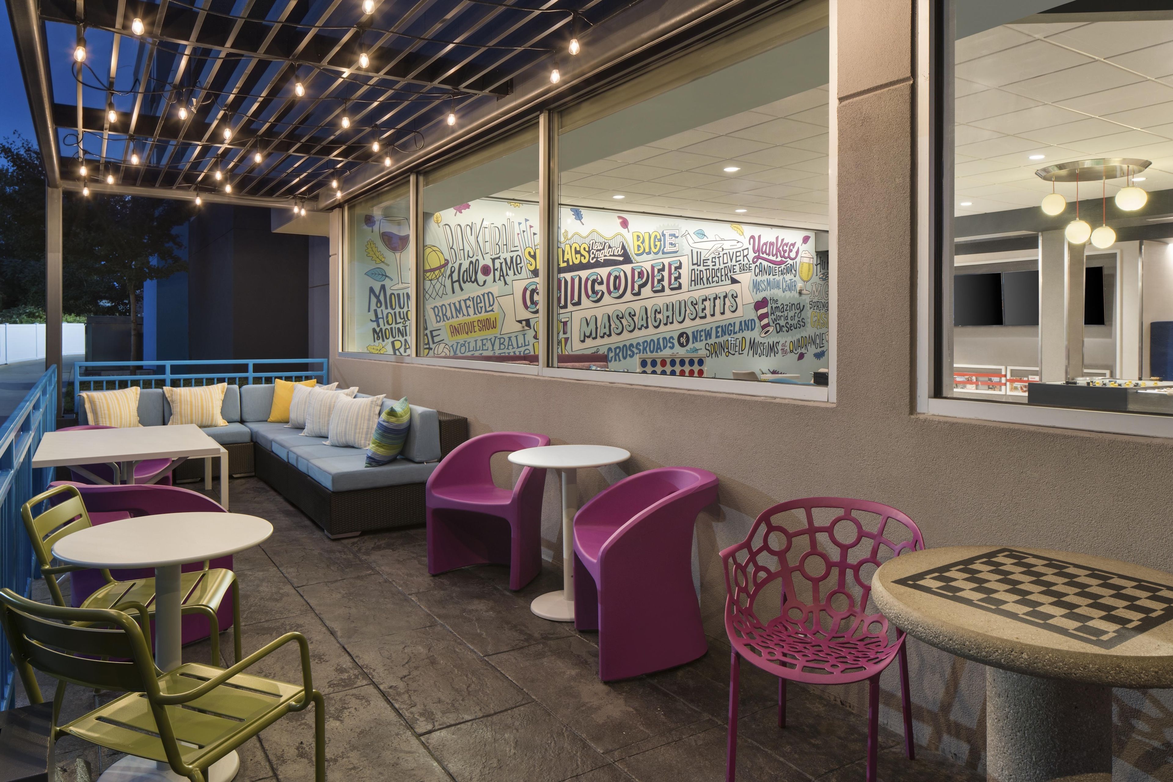 An outdoor seating area with tables and chairs, a sofa, and a large window with various text and graphics.