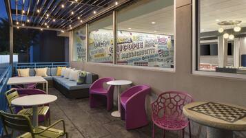An outdoor seating area with tables and chairs, a sofa, and a large window with various text and graphics.