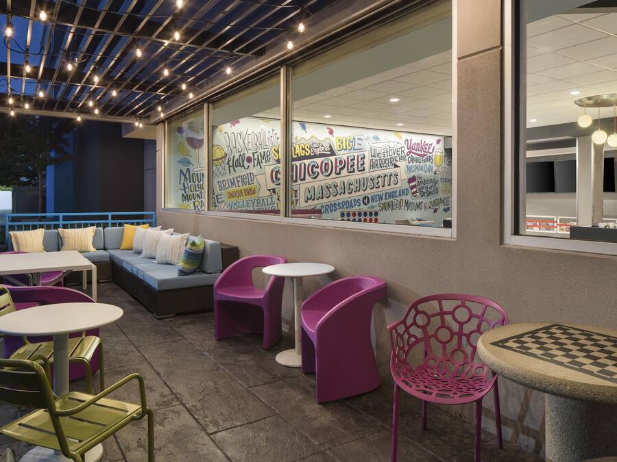 An outdoor seating area with tables and chairs, a sofa, and a large window with various text and graphics.