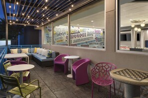 An outdoor seating area with tables and chairs, a sofa, and a large window with various text and graphics. - Tru by Hilton Chicopee Springfield (Chicopee)