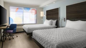 A hotel room with two beds, a desk, a chair, and a TV.