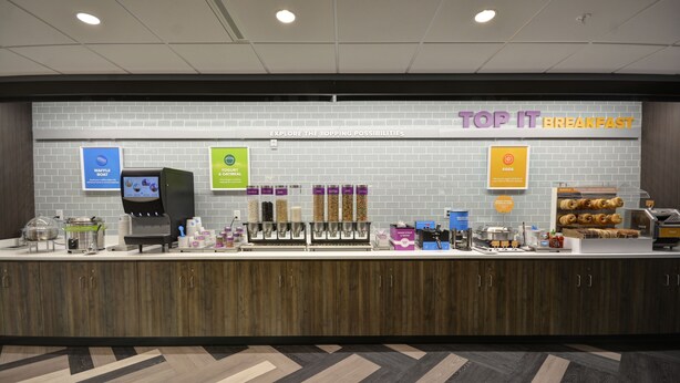 A breakfast area with a waffle station, coffee machine, and various food options. - Tru by Hilton Chicopee Springfield (Chicopee)