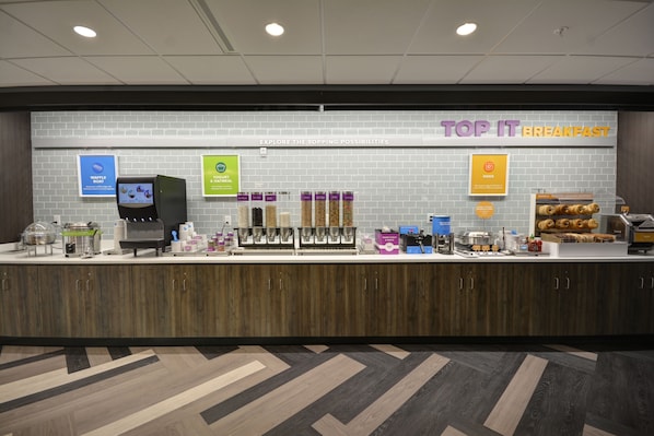 A breakfast area with a waffle station, coffee machine, and various food options. - Tru by Hilton Chicopee Springfield (Chicopee)