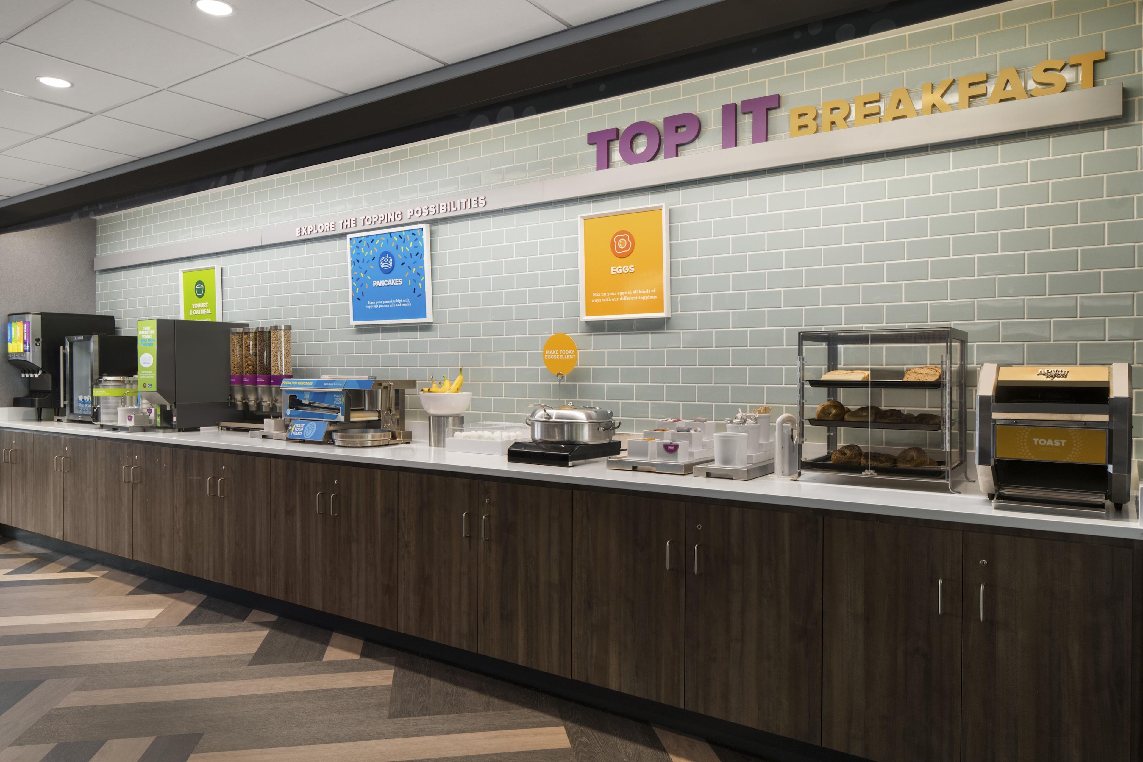 A breakfast buffet area with a sign reading 'TOP IT BREAKFAST' and various food items displayed.