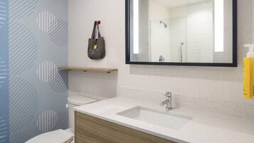 Une salle de bain avec des toilettes blanches, un lavabo surmonté d’un miroir et un distributeur de serviettes fixé au mur.