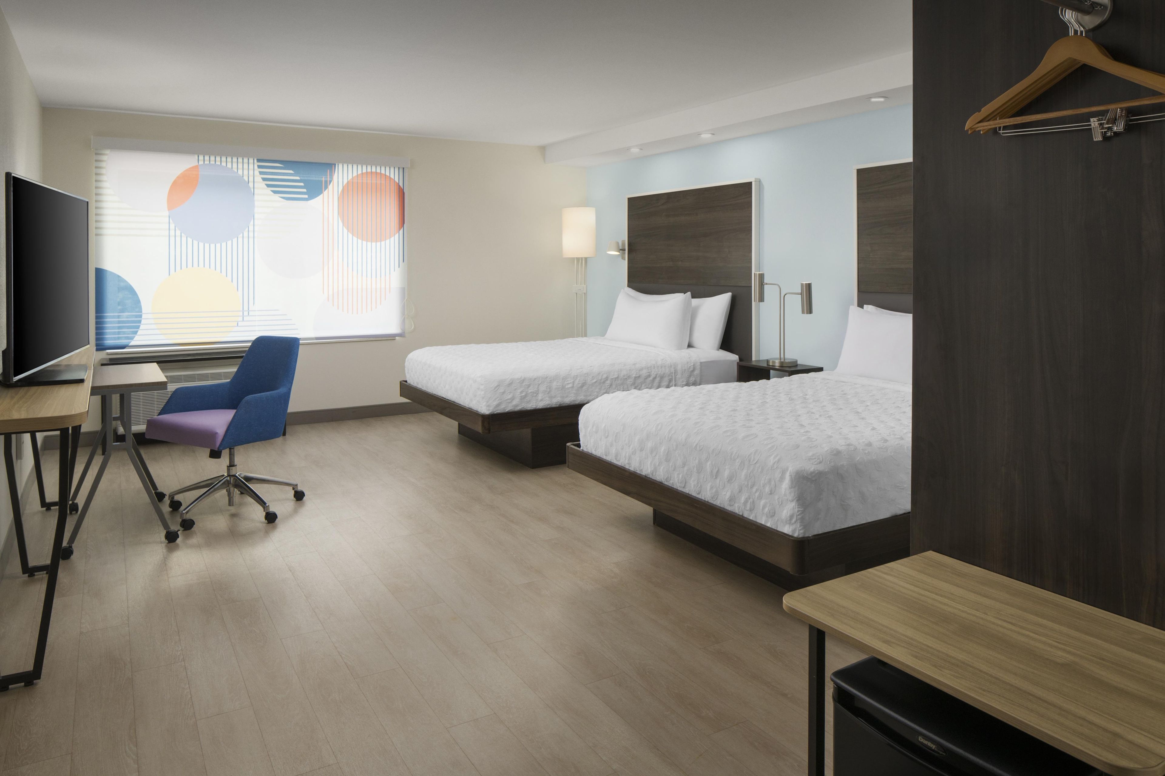 A hotel room with two beds, a desk with a chair, a television, and a window with blinds.