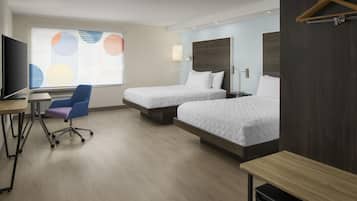 A hotel room with two beds, a desk with a chair, a television, and a window with blinds.