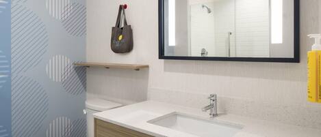 A bathroom with a white toilet, a sink with a mirror above it, and a towel dispenser on the wall.