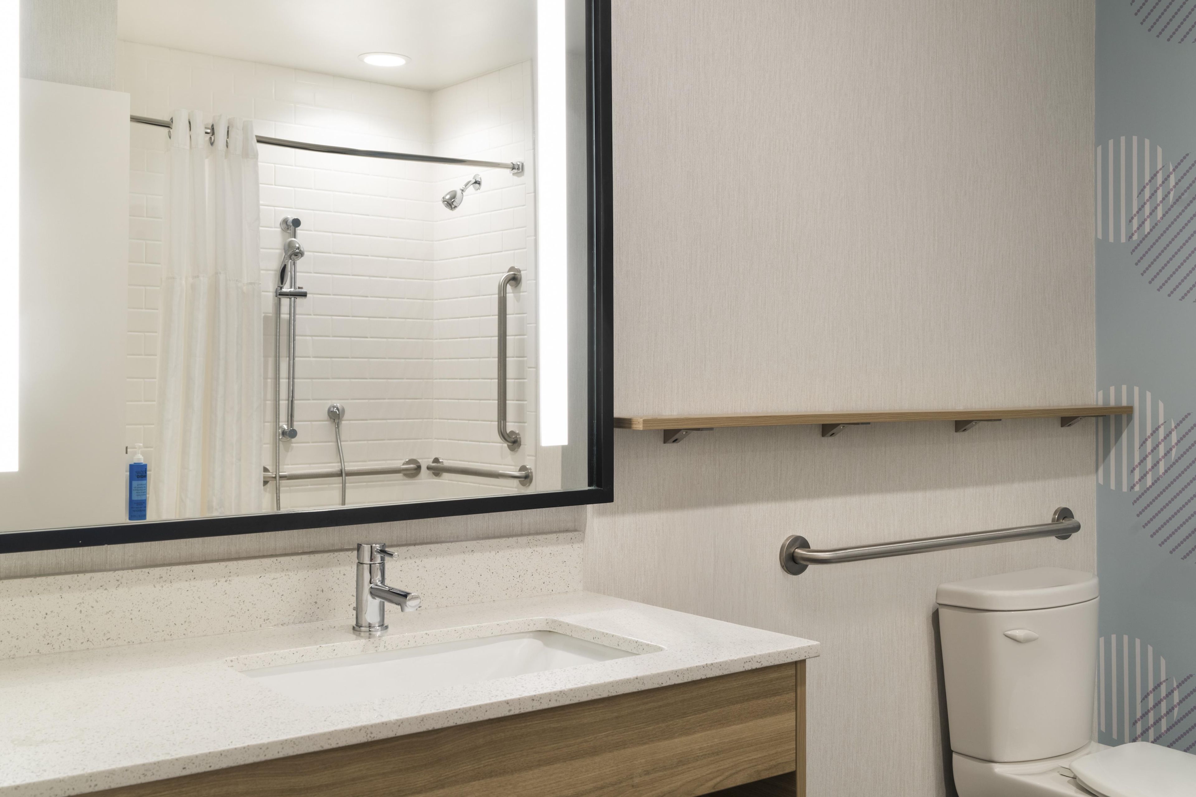 A bathroom with a white sink, a mirror, a shower with grab bars, and a toilet with a grab bar.