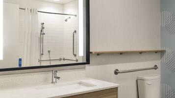 A bathroom with a white sink, a mirror, a shower with grab bars, and a toilet with a grab bar.