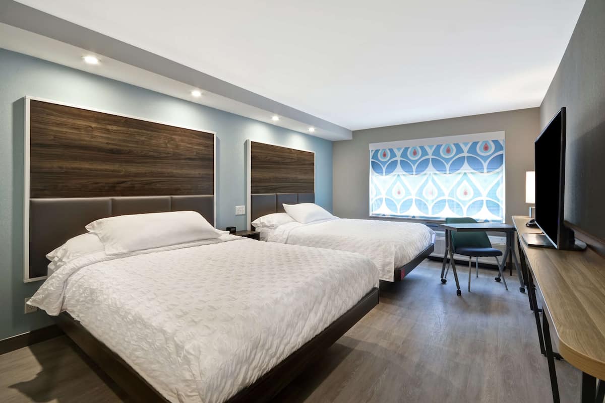 Habitación de hotel con dos camas, un escritorio y un televisor.