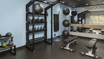 Un gimnasio con una estructura para sentadillas, mancuernas kettlebell, balones medicinales y una banca.