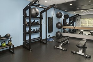Un gimnasio con una estructura para sentadillas, mancuernas kettlebell, balones medicinales y una banca.