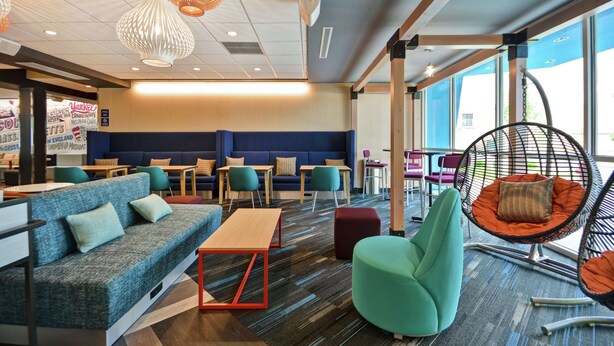 A modern lounge area with seating options including sofas, chairs, and a hanging chair. Tables and a counter are also visible. - Tru by Hilton Chicopee Springfield (Chicopee)