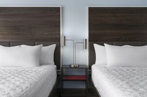 Una habitación de hotel con dos camas, una mesita de noche y una lámpara moderna.
